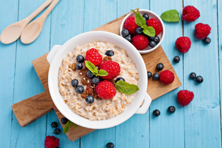 Oatmeal oprridge with fresh raspberry and blueberry on bright blue background. Healthy breakfast for children and parents. Tasty vegetarian food.の写真素材
