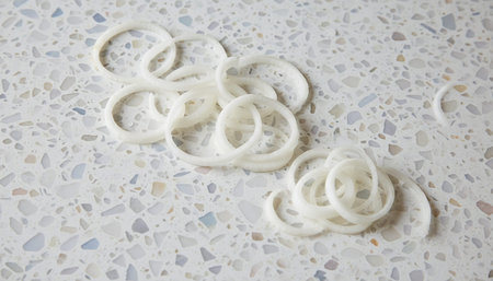 A close-up view of thinly sliced white onion rings arranged on a textured surface, showcasing their freshness and potential use in various culinary applications.