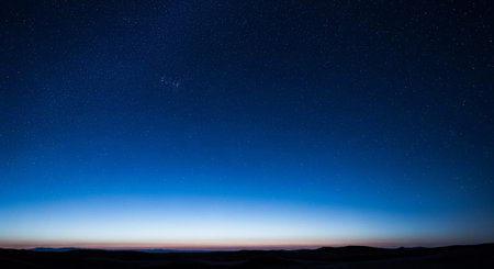 The night sky is a canvas of stars, with a deep blue hue that fades into the horizon. The landscape below is silhouetted against the celestial backdrop, creating a serene and captivating scene.