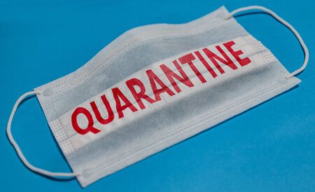 Medical face mask with QUARANTINE text on blue background. Concept of coronavirus quarantine.の写真素材