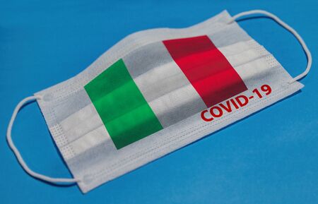 Medical face mask with  flag of Italy and COVID-19 text on blue background. Concept of coronavirus quarantine.の写真素材