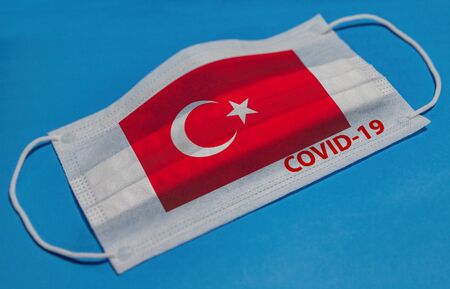Medical face mask with  flag of Turkey and COVID-19 text on blue background. Concept of coronavirus quarantine.の写真素材