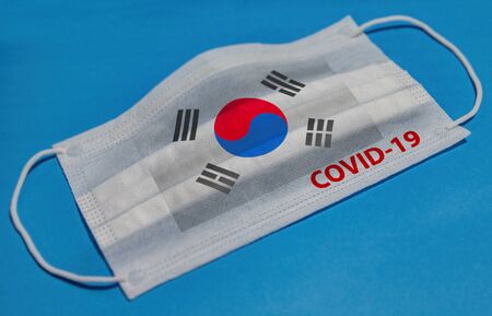 Medical face mask with  flag of South Korea and COVID-19 text on blue background. Concept of coronavirus quarantine.の写真素材