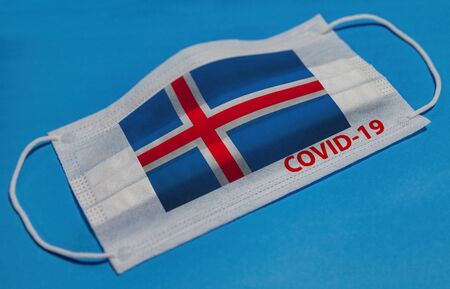 Medical face mask with  flag of Iceland and COVID-19 text on blue background. Concept of coronavirus quarantine.の写真素材