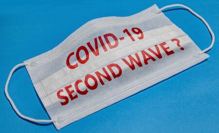 Medical face mask with COVID-19 SECOND WAVE text on blue background. Concept of coronavirus quarantine.の写真素材