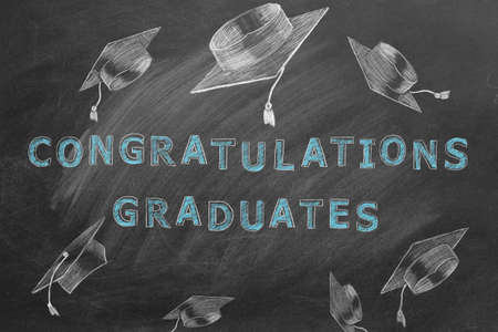 Hand drawing text CONGRATULATIONS GRADUATES and graduation caps on blackboard.