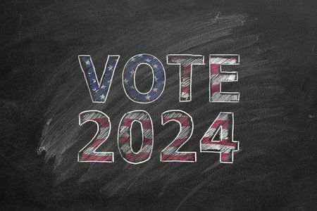 The inscription VOTE 2024 In the colors of the American flag is drawn with chalk on a blackboard. US...
