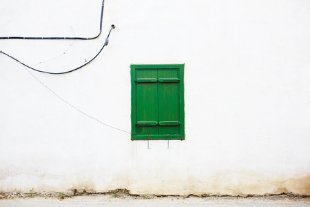 Old mediterranean italian style green window on a cracked white wall with cords. Closed shutters.の写真素材