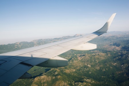 Airplane wing view from the window flying above green mountainsの写真素材