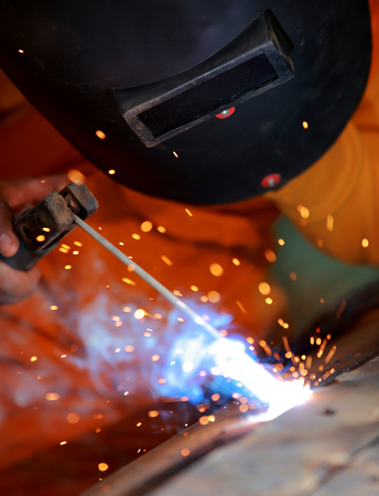 Close-up worker with protective mask welding metal.