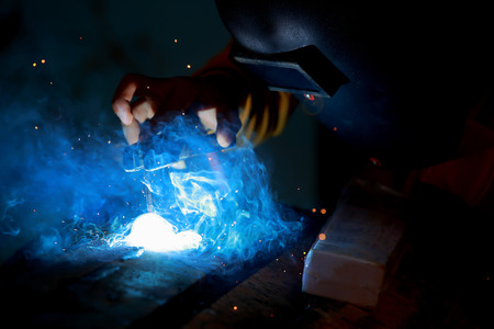 Close-up worker with protective mask welding metal.