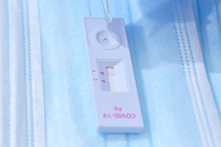 Woman wearing blue medical gloves and holding COVID-19 (SARS-CoV-2) First Antigen Test kit device to...