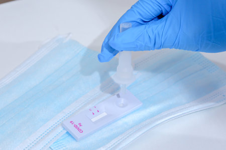 Woman wearing blue medical gloves and holding COVID-19 (SARS-CoV-2) First Antigen Test kit device to...