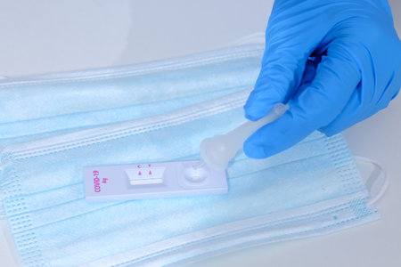 Woman wearing blue medical gloves and holding COVID-19 (SARS-CoV-2) First Antigen Test kit device to...