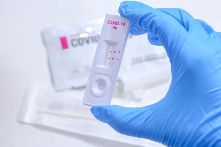 Woman wearing blue medical gloves and holding COVID-19 (SARS-CoV-2) First Antigen Test kit device to help in the Rapid Detection testing at home. Showing positive COVID-19 outbreak.の写真素材
