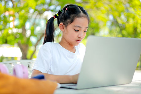 Little kid girl asian uses a laptop to learn at school. The child smiles happily and gets knowledge remotely. which enhances the classroom learning skills. Concept Back to school.の写真素材
