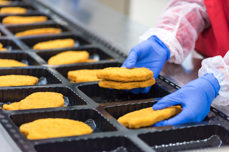 The worker in the factory places the chicken schnitzelの写真素材