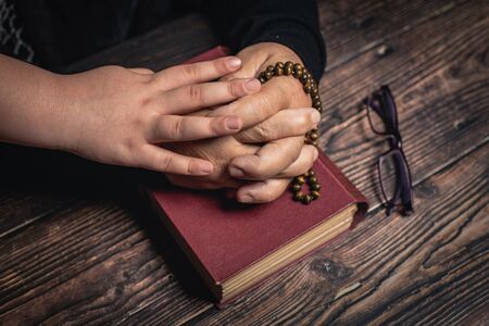 Girl and Old Woman with closed hands holding rosary on holy book staying at home and praying for...