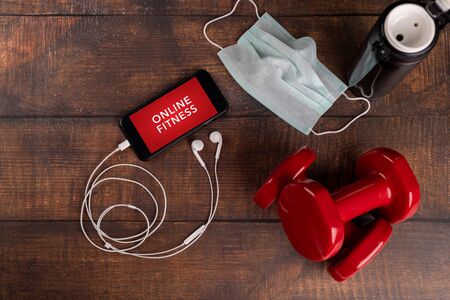Red dumbbell and smartphone on a woodan background. App for training indoors. Online Fitness...