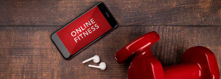 Red dumbbell and smartphone on a woodan background. App for training indoors. Online Fitness program. Home online workout. Top view, Covid-19 Coronavirus quarantine conceptの写真素材