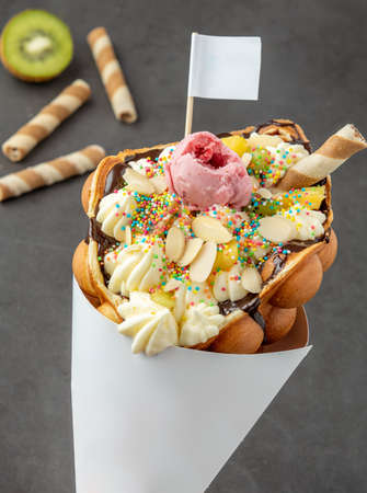 Hong kong or bubble waffle with ice cream, fruits, chocolate sauce and colorful candyの写真素材