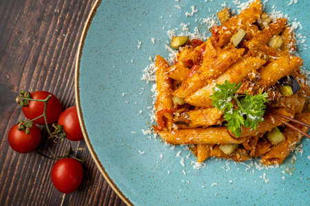 Penne pasta in tomato sauce, tomatoes decorated with parsley on a wooden background