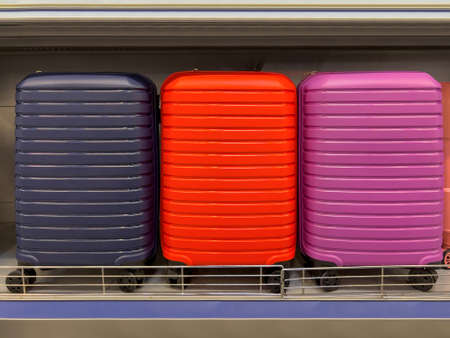 Modern wheeled suitcase in 3 different colors on display on the store shelfの写真素材