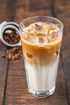 A cup of Iced Latte Coffee with ice cubes placed on a wooden table in a coffee shop