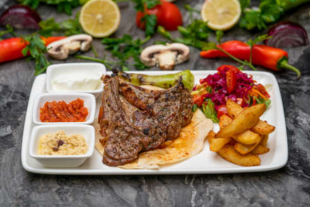 Grilled lamb chops with french fries and appetizers on a white porcelain plate