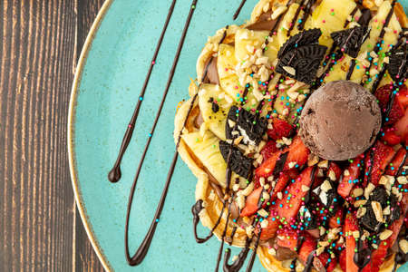 Heart waffle with pineapple and strawberry with gummy candy and ice cream on it.