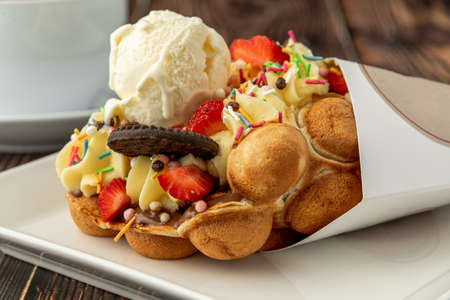 Hong kong or bubble waffle with ice cream, fruits, chocolate sauce and colorful candyの写真素材