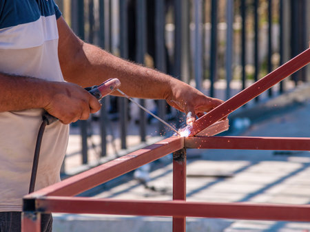 Welder welding two iron profiles at the construction site on a sunny dayの写真素材