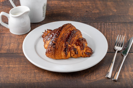 Croissant with coffee next to it on wooden tableの写真素材