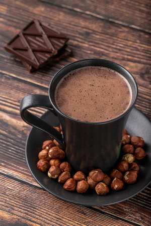 Hazelnut hot chocolate with chocolate next to it on wooden tableの写真素材