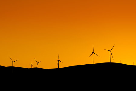 Multiple wind turbines standing on a hill at sunset and generating electricityの写真素材