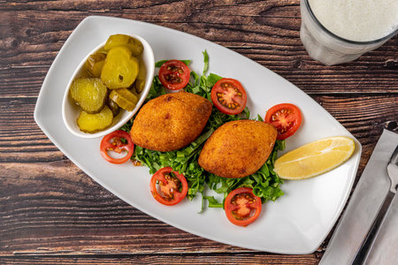 Kibbeh or icli kofte on a white porcelain plate with pickles and saladの写真素材