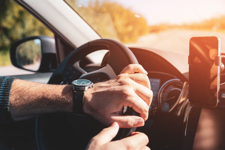 Man with both hands on steering wheel driving at sunset