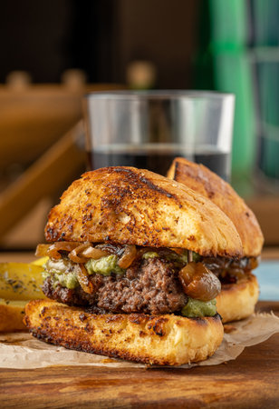 Caramelized onion burger with avocado sauce cut in half, with sauces and french fries on the sideの写真素材