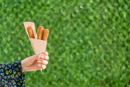 woman holding churros in cardboard box in front of green grass wall