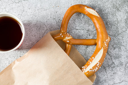 Pretzel wrapped in wrapping paper with drink next to it on stone table