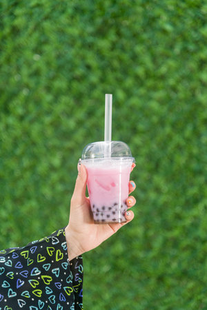 Woman holding bubble tea with lemonade in front of green grass wallの写真素材