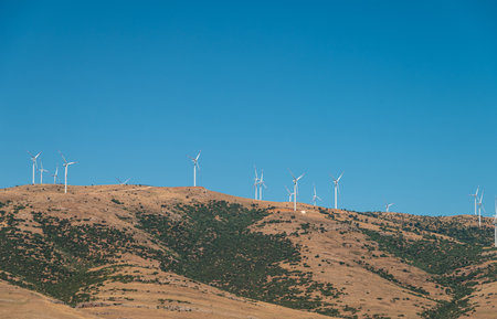 Wind turbines standing on a hill and generating electricity at sunny blue sky