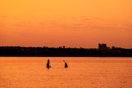 Adventurous people on a stand up paddle board is paddling during a bright and vibrant sunriseの写真素材