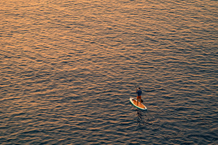 Adventurous people on a stand up paddle board is paddling during a bright and vibrant sunrise