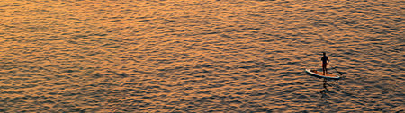 Adventurous people on a stand up paddle board is paddling during a bright and vibrant sunrise