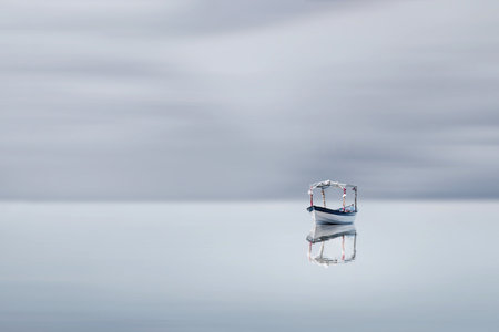 Fine art image of a fishing boat floating on a cloudy river, taken with long exposure techniqueの写真素材
