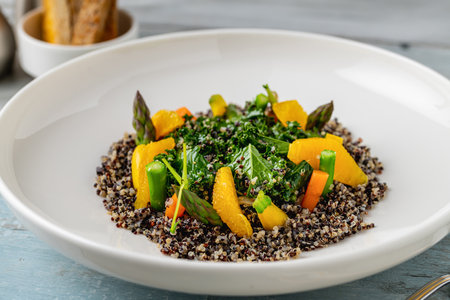 Quinoa salad with orange and kale leaves on white porcelain plate on wooden tableの写真素材