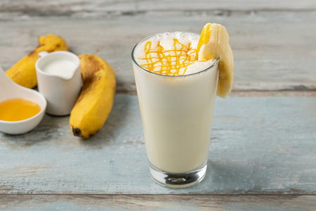 Milk with honey and banana in glass on wooden tableの写真素材