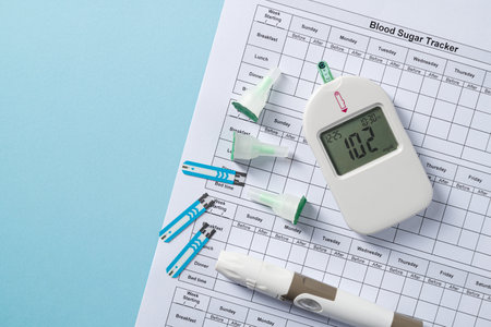 Top view of glucometer, lancet pen, strips and blood sugar tracker on blue background. diabetes test...