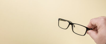 Hand holding black framed prescription glasses in front of yellow backgroundの写真素材